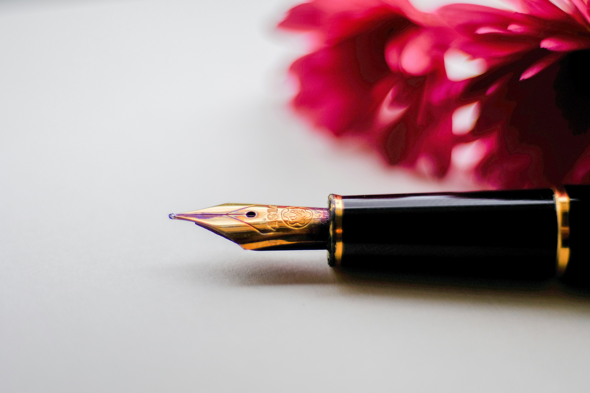 fountain pen laying on a white table with pink flower in the background